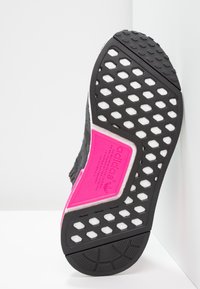 Svart och rosa idrottssko sula med en texturerad gummidesign som har hexagonala utskärningar och framträdande varumärkeslogotyp på en plan yta.