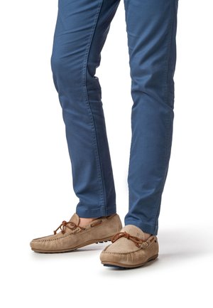 Chaussures style mocassin en daim fauve avec des lacets marron, portées avec un pantalon bleu slim fit doté de poches latérales et d'une finition lisse.