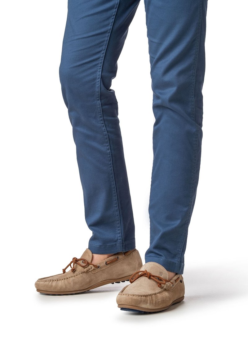 Chaussures style mocassin en daim fauve avec des lacets marron, portées avec un pantalon bleu slim fit doté de poches latérales et d'une finition lisse.