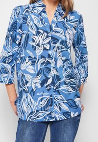 Blue button-up shirt with white floral patterns, 3/4 sleeves, and a collar. Made of lightweight fabric with a smooth texture.