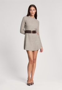 Robe in maglia color beige chiaro, texture a costine, con maniche lunghe e una cintura marrone con fibbia metallica, abbinata a scarpe flat a punta.