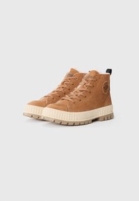 Baskets montantes en daim marron avec une semelle en caoutchouc texturé beige, des lacets assortis et une languette. Présente un logo circulaire sur le côté.