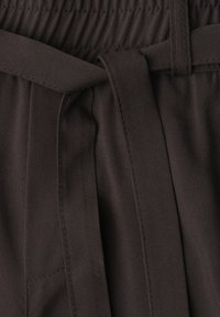 Gros plan sur un pantalon en tissu foncé avec une taille élastique et une ceinture en tissu nouée à l'avant.