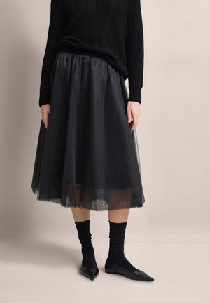 Black tulle skirt with a voluminous design, layered fabric, and textured finish. Paired with a black knit sweater, black socks, and pointed flats.