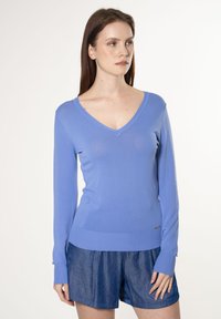 Lichtblauwe V-hals trui van zacht gebreid materiaal, met lange mouwen en een geribde onderrand, gecombineerd met denim shorts.