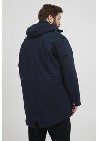 Mørkeblå, hetteparka med avslappet passform. Har snor i kanten og trykknapper på ermene for justering. Glatt stofftekstur.