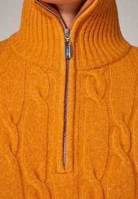 Maglione arancione a maglia con colletto a coste alto, chiusura frontale con zip a metà e dettaglio in punto cavallo. Finissaggio in tessuto liscio.