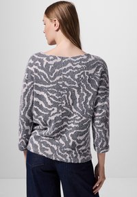 Weicher, gestrickter Pullover in Grau und zartem Rosa mit einem zebraähnlichen Muster, weitem Ausschnitt und Dreiviertelärmeln, kombiniert mit dunklen Jeans.