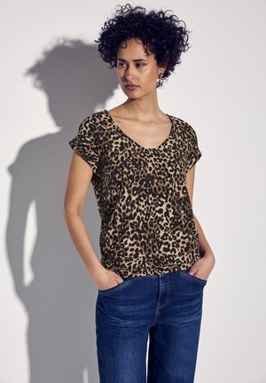 Leopard print short-sleeve top in tan and black, featuring a V-neck, paired with blue jeans. Soft fabric with a relaxed fit.