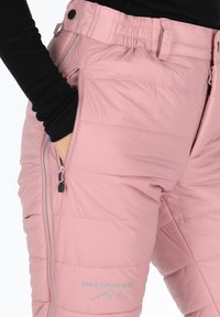 Roze geïsoleerde broeken met een gequilt ontwerp, voorzien van een ritszak en een elastische tailleband. Logo gedrukt op de voorkant.