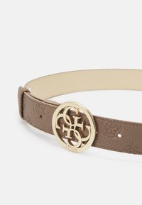 Rudas odinis diržas su tekstūruotu paviršiumi, turintis didelį auksinės spalvos apvalų sagtį su prekės ženklu "Guess". Papuoštas logotipo raštais.