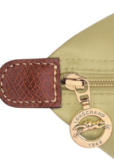 Green nylon pouch with brown leather accent, gold zipper, and circular metal tag featuring the Longchamp logo and "1948" embossed.