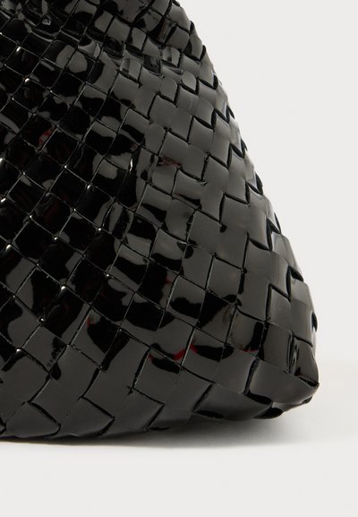 Juodasis austas rankinukas su blizgiu paviršiumi, išskirtiniais kvadratiniais raštais ir lygiu tekstūru. Apvalus forma pabrėžia jo profilį.