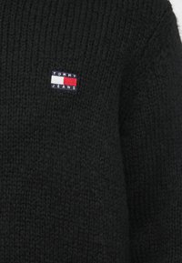 Czarny sweter dzianinowy z prążkowaną teksturą, z małym haftowanym logo w kolorach czerwonym, białym i niebieskim od Tommy Jeans.