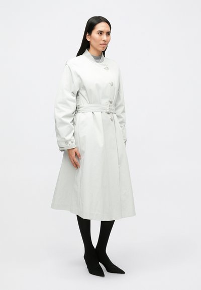 Világosszürke ballonkabát övvel a deréknál, dupla soros gombokkal és légies sziluettel. A modell fekete harisnyát és hegyes orrú cipőket visel.