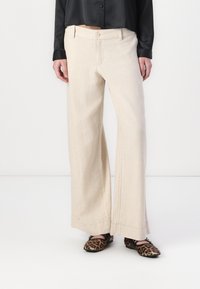Pantalon large beige en tissu léger, avec poches avant et fermeture à bouton, associé à des ballerines à imprimé léopard.