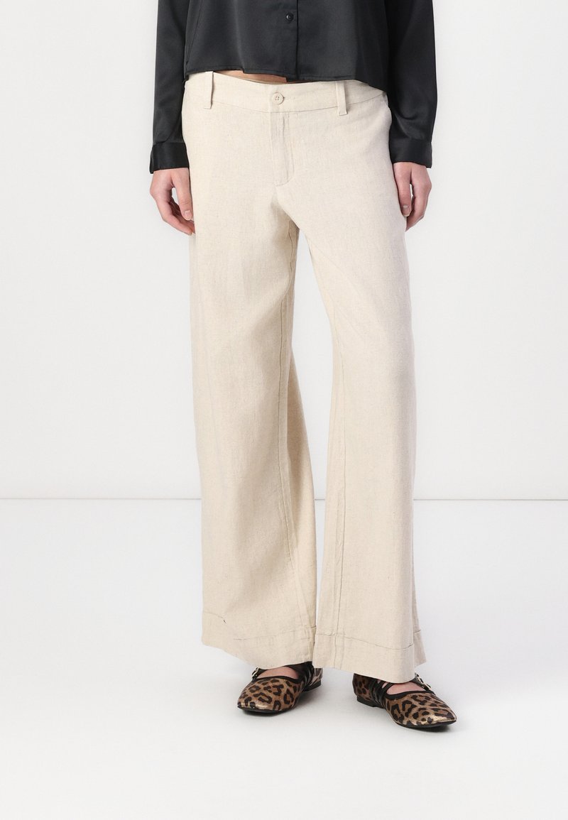 Pantalon large beige en tissu léger, avec poches avant et fermeture à bouton, associé à des ballerines à imprimé léopard.