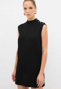 Vestido negro sin mangas con un escote elevado, que presenta detalles de botones en el hombro. Tela suave y corte entallado.