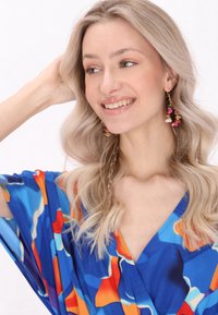 Värikäs sininen mekko, jossa on abstrakteja kuvioita punaisena, oranssina ja tealina; kevyttä kangasta, jossa on rento istuvuus ja leveät hihat; kultaketjut koristeellisilla yksityiskohdilla.