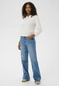 Pull blanc en tricot avec un motif texturé, et jeans larges bleus. Le pull présente un col et des manches trois-quarts.