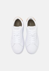 Weiße synthetische Sneaker mit runden Zehen, flachen Schnürsenkeln und einem beigen Akzent an der Ferse. Logo sichtbar an der Seite und im Innenfutter.