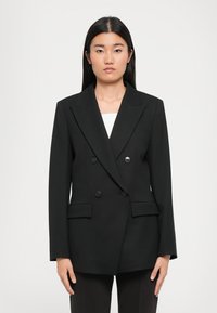 Svart dobbeltspent blazer med brede revers, to frontlommer og runde svarte knapper. Skreddersydd passform med lange ermer og strukturert design.