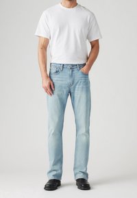 Jean bleu clair à coupe droite, porté avec un t-shirt blanc uni. Le jean présente un design classique à cinq poches.