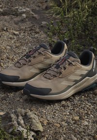Beżowe buty trekkingowe z siateczkową cholewką, ciemnoszare akcenty, teksturowana gumowa podeszwa i wzmocniony czubek dla zwiększonej trwałości. Wyposażone w system sznurowania.