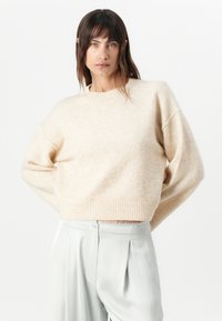 Cream wool blend sweater with a ribbed hem and wide sleeves. Paired with light gray, smooth, pleated trousers. Simple, contemporary design.