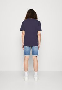 T-shirt blu navy a maniche corte, abbinato a pantaloni corti in denim azzurro chiaro, leggermente arrotolati all'orlo. Calzini bianchi e sneaker completano il look.