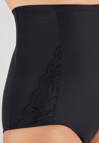 Perizoma nero a vita alta in tessuto morbido, con un motivo in pizzo dettagliato sul lato sinistro e un design senza cuciture per il massimo comfort.
