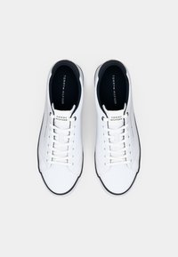 Paire de baskets basses blanches Tommy Hilfiger avec lacets blancs et semelles intérieures noires, vue de dessus sur un fond clair.
