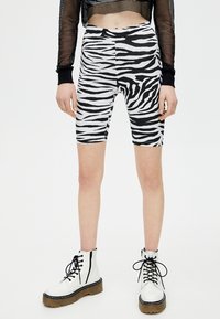 Zwart-wit zebra print fietsbroekjes van rekbaar materiaal, met een hoge taille en een aansluitende pasvorm, die net boven de knie eindigen.