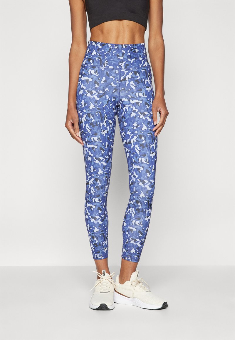 Blå camouflagemönstrade leggings gjorda av stretchy material, med hög midja och avsmalnande passform, i kombination med ljusa träningsskor.