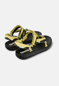 Yellow and black sandal with textured black sole, featuring adjustable straps in a geometric pattern and a prominent logo on the footbed.