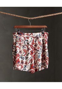 Pantalones cortos florales en color crema, con un patrón de flores rojas y azules, cintura alta, pliegues y bolsillos traseros. Textura de tela lisa.