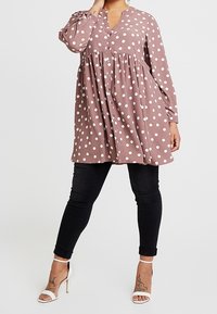 Hnědá halenka s puntíky, s véčkovým výstřihem, dlouhými rukávy, nabíranou částí a zapínáním na knoflík. Kombinována s černými skinny džíny a sandály na vysokém podpatku.