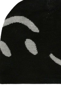 Czarna dziana czapka z dużymi białymi abstrakcyjnymi kształtami przypominającymi oczy i brwi wydzierganymi w materiał.