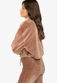 Casaco cropped castanho de veludo cotelê com textura canelada, apresentando mangas oversized e bainha elástica, combinado com calças slim-fit a condizer.