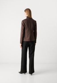 Hnědý oblekový blazer s úzkým střihem, s knoflíkovými manžetami a hladkou texturou, kombinovaný s černými širokými kalhotami.