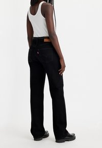 Vaqueros de denim negros con corte recto, con un parche de cuero en la cintura trasera, detalles sutiles de costuras y bolsillos laterales.