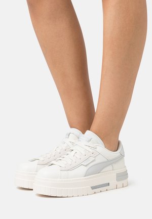 Baskets en cuir blanc avec une semelle plateforme épaisse, des accents texturés et des détails gris clair sur les côtés. Les lacets sont plats et bien visibles.