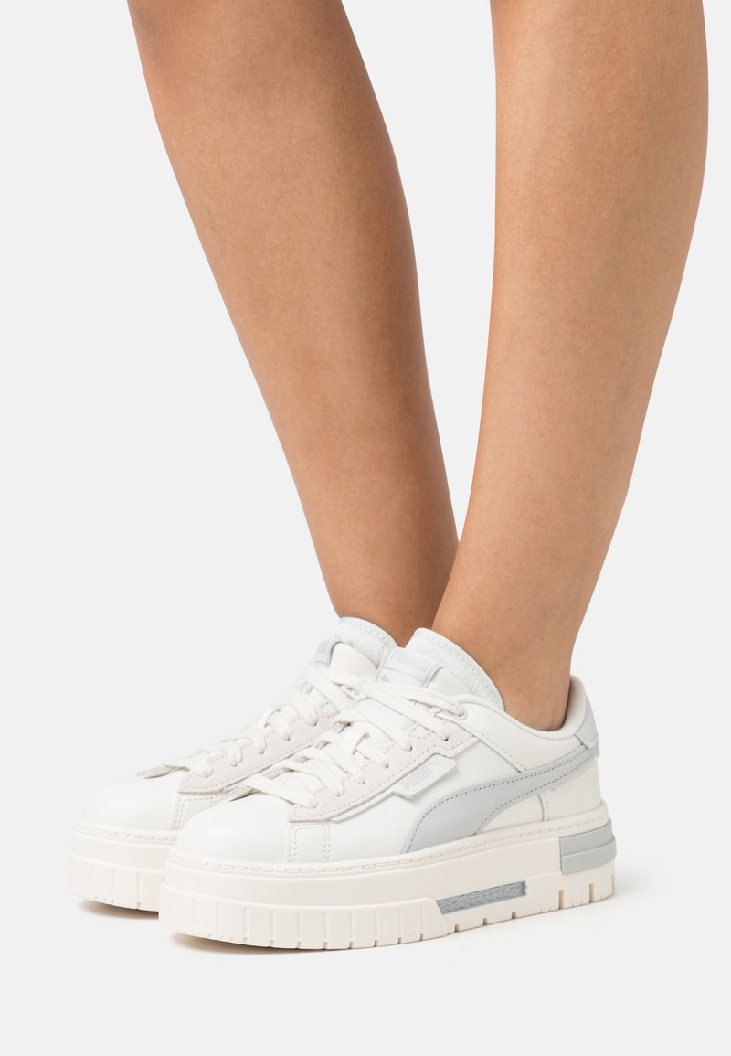 Sneakers bianchi in pelle con suola a piattaforma spessa, dettagli texturizzati e particolari grigio chiaro sui lati. I lacci sono piatti e ben visibili.
