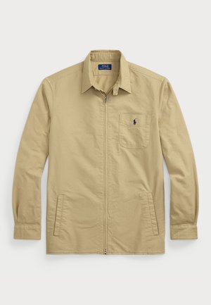 Light beige zip-up jacket with long sleeves, point collar, front pockets, and a small embroidered logo above the left pocket. Cotton material.