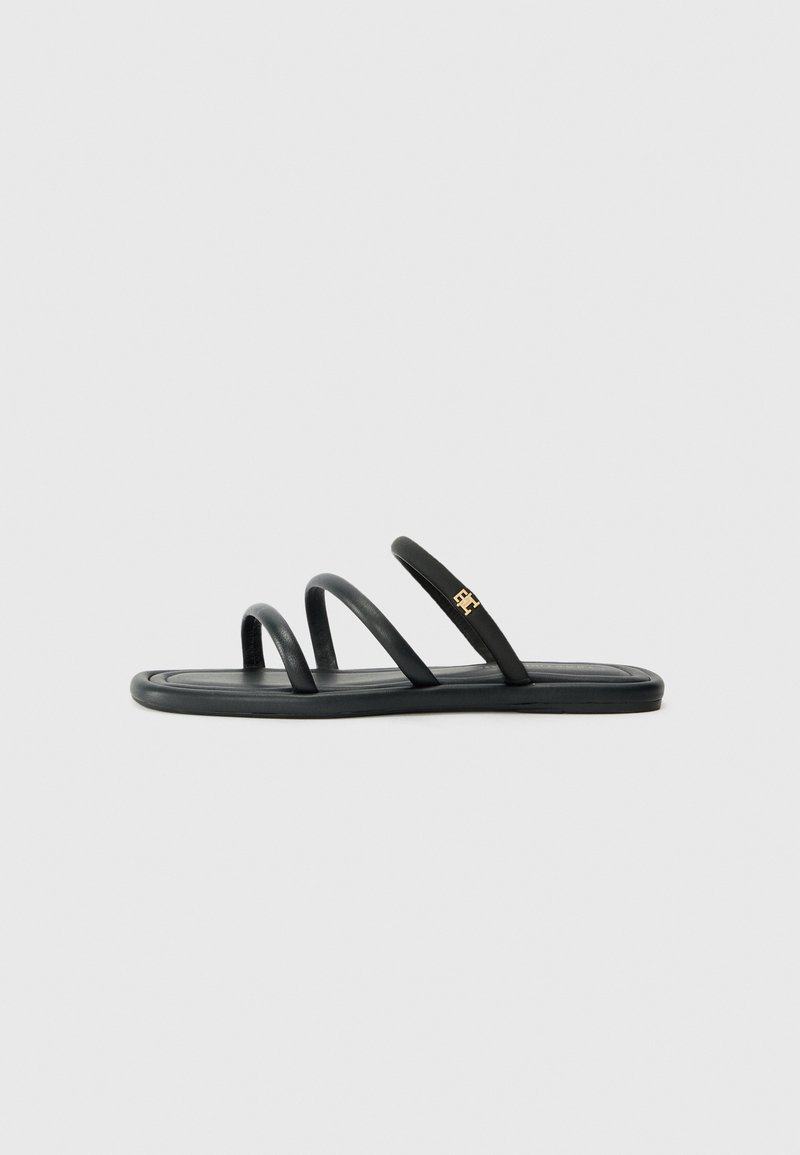 Svarta platta sandaler med tre smala remmar och en guldig logotypaccent. Slät textur och minimalistisk design, med en platt sula.