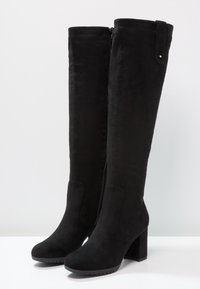 Botas negras sobre la rodilla, hechas de suave ante, con cremallera lateral, tacón cuadrado y diseño de punta redonda. Textura suave con un diseño minimalista.