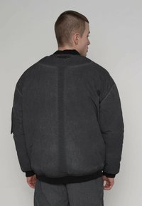 Zwarte gewatteerde jas van gestructureerde stof, met een ronde halslijn, geribbelde manchetten en een naaddetail aan de achterkant. Minimalistisch ontwerp.