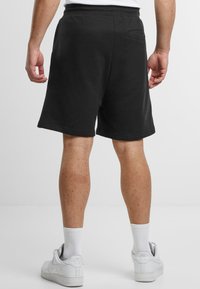 Mustat puuvillaiset college-shortsit, joissa on joustava vyötärö, kaksi sivutaskua ja takatasku, yhdistetty valkoisiin lenkkarit ja miesten sukat.