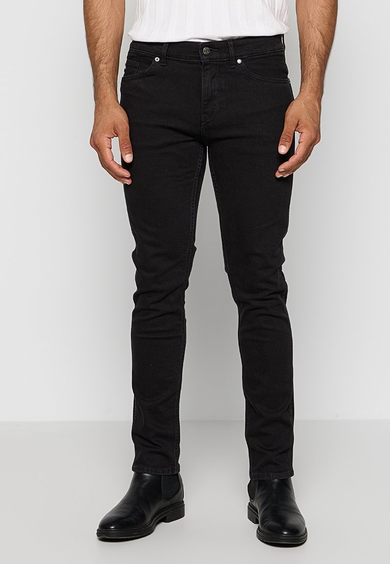 Jeans noirs ajustés avec un design à cinq poches, fermeture à glissière et détails de couture subtils. Le matériau est du denim avec une texture lisse.