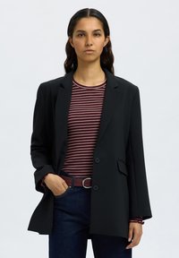 Svart blazer med skreddersydd design, med en enkelt knappelukking og to frontlommer, kombinert med en burgunderstripete skjorte og jeans.